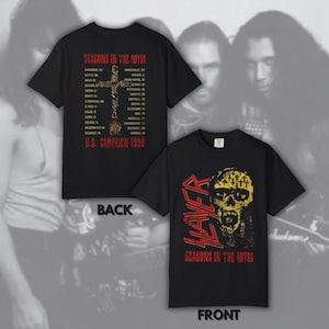May include: A black short-sleeved t-shirt featuring a Slayer graphic on the front with a yellow skull and red text reading Seasons in the Abyss. The back displays a list of cities from the 1990 U.S. Campaign tour with a cross graphic and red text.