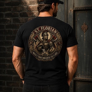 May include: A black t-shirt featuring a circular graphic on the back. The design depicts Saint Florian in armor pouring water on flames, flanked by two axes. The text reads ST. FLORIAN and PROTECT THOSE WHO ENTER THE FLAMES in a circular border.