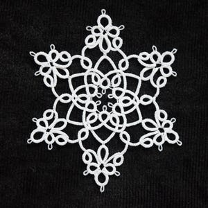 May include: A white, six-pointed snowflake doily with intricate lace detailing. The delicate design features looped patterns and floral-like shapes, set against a dark, textured background. This handcrafted item is perfect for winter decor.