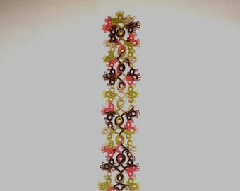May include: A vertical strip of tatting lace featuring a repeating floral-inspired pattern. The design is composed of interconnected loops and rings in shades of dark brown, olive green, coral pink, and cream, creating a delicate, intricate texture.