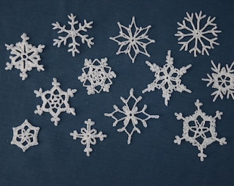 Op de afbeelding: Een verzameling witte, gehaakte sneeuwvlokken van verschillende groottes en ontwerpen op een donkerblauwe achtergrond. De sneeuwvlokken hebben ingewikkelde patronen en delicate details, perfect voor winterse knutselwerken of decoraties.