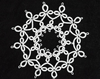 Op de afbeelding: Een witte, cirkelvormige doily met een delicaat, kantachtig ontwerp. Het ingewikkelde patroon bevat herhaalde bloemen en lusvormige elementen, waardoor een symmetrisch, open ontwerp ontstaat tegen een zwarte achtergrond. De doily is waarschijnlijk handgemaakt.