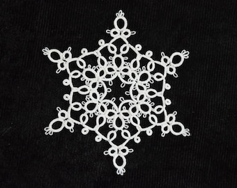 Op de afbeelding: Een wit sneeuwvlokontwerp tegen een zwarte achtergrond. De sneeuwvlok is gemaakt van ingewikkelde, onderling verbonden lussen en vormen, waardoor een sierlijk, sierlijk uiterlijk ontstaat. Het ontwerp is symmetrisch en gedetailleerd.