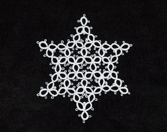 Op de afbeelding: Een witte, stervormige kanten doily op een zwarte achtergrond. De doily is gemaakt met een delicaat, herhalend bloemmotief, waardoor een symmetrisch, open ontwerp ontstaat. Het contrast tussen het witte kant en de zwarte achtergrond benadrukt het vakmanschap.
