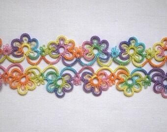 May include: A length of multicolored tatting lace trim featuring a repeating pattern of interconnected floral motifs. The lace is crafted from fine thread in vibrant shades of orange, yellow, green, blue, purple, and pink, forming a delicate border.