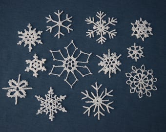 Op de afbeelding: Een verzameling witte, gehaakte sneeuwvlokken van verschillende maten en ontwerpen, gerangschikt op een donkerblauwe achtergrond. De sneeuwvlokken hebben ingewikkelde patronen, die lijken op natuurlijke ijskristallen, perfect voor winterse knutselwerken en decoraties.