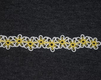 Op de afbeelding: Een witte en gele madeliefjesketting. De rand heeft een herhalend patroon van madeliefjes met witte bloemblaadjes en gele centra. De rand wordt weergegeven tegen een donkergrijze achtergrond.