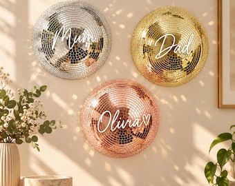 May include: Three circular disco ball wall decorations in silver, gold, and rose gold. The silver ball features the white text Mum, the gold ball features the white text Dad, and the rose gold ball features the white text Olivia with a heart.