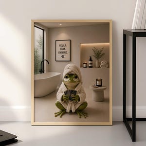 Puede incluir: Una lámina artística enmarcada que muestra una rana verde con albornoz blanco y una toalla en la cabeza, sosteniendo cartas en un baño. El baño incluye una bañera blanca, una mesa pequeña con una vela y un cartel que dice RELAX. SOAK. UNWIND.