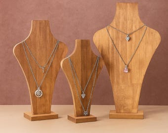 Op de afbeelding: Drie houten sieradenstandaards met zilveren kettingen. Elke standaard bevat meerdere kettingen met verschillende hangerontwerpen, waaronder een bloem, een hart en een edelsteen. De standaards staan tegen een neutrale achtergrond.