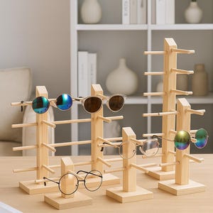 Puede incluir: Expositores de madera para gafas de sol con varios pares de gafas de sol y gafas. Los expositores son de madera clara y tienen múltiples clavijas horizontales para sujetar las gafas. Las gafas incluyen modelos redondos, aviador y ojo de gato.