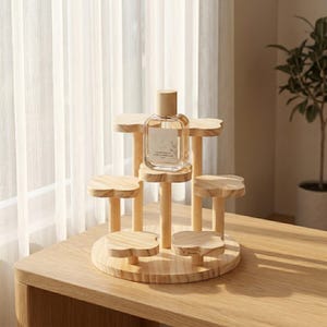 Op de afbeelding: Een gelaagde displaystandaard van lichtgekleurd hout met een ronde voet en meerdere klavervormige plateaus op verschillende hoogtes. Een doorzichtig glazen parfumflesje met een rechthoekig etiket staat op het bovenste centrale plateau.
