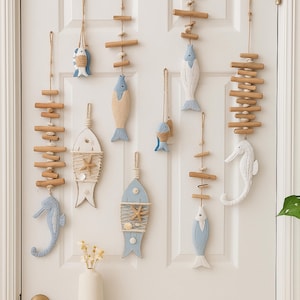 Op de afbeelding: Wanddecoratie met een kustthema met houten vissen, zeepaardjes en drijfhoutaccenten. De vissen zijn geschilderd in blauw- en wittinten, sommige versierd met zeesterren en touw. De decoraties hangen aan touw, wat een nautische esthetiek creëert.