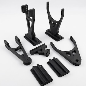 Puede incluir: Un conjunto de componentes de nailon negro relleno de carbono que incluye dos soportes verticales con múltiples orificios de ajuste, dos placas de montaje planas con rieles ranurados, una pieza de pivote en ángulo y dos segmentos de brazo triangulares.