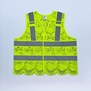 May include: A neon yellow safety vest with a floral lace pattern. The vest has gray reflective stripes and accents, with a scalloped hemline. The vest has a button closure and shoulder straps.