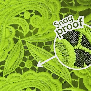 Op de afbeelding: Close-up van een fel neon groene stof met ingewikkelde bloemenborduurwerk. De stof heeft een mesh achterkant en de woorden "Snag Proof" worden weergegeven in een witte cirkel.