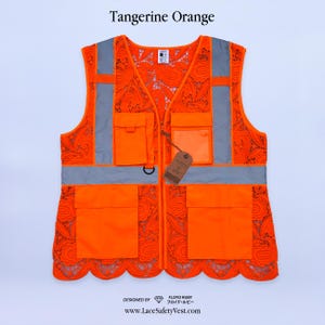 Può includere: Gilet di sicurezza arancione mandarino con strisce riflettenti e dettagli in pizzo. Presenta più tasche e una chiusura con cerniera. Il gilet ha il testo "Tangerine Orange" in alto e "Designed by Floyd Ruby" in basso.