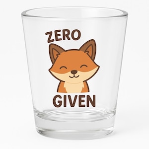 May include: A clear shot glass with the words "ZERO GIVEN" and a cartoon fox illustration. The fox is orange and brown with a smiling face. The text is in a bold, sans-serif font.