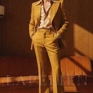 May include: Mustard yellow suit with a matching jacket and flared pants. The suit is paired with a patterned button-down shirt. The image features a retro aesthetic, with a brown sofa and wooden paneling in the background.