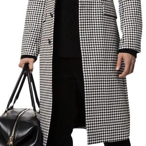 Könnte beinhalten: Ein schwarz-weißes Mantel mit Hahnentrittmuster, dazu ein schwarzer Rollkragenpullover und eine schwarze Hose. Die Person hält eine schwarze Leder-Reisetasche und trägt schwarze Stiefel.