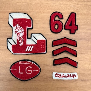 May include: A collection of red and white embroidered patches including a large letter L with a football player graphic, the number 64, three chevron stripes, an oval patch with the text LG, and a rectangular patch with the text C.F.smithjr.