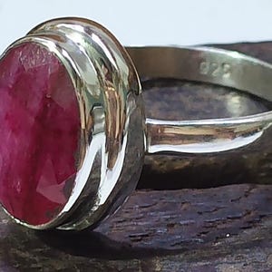 May include: A sterling silver ring featuring a large, oval-cut ruby gemstone. The ruby is a deep, vibrant red color, set in a polished silver band. The ring is stamped with "925" indicating the silver purity.