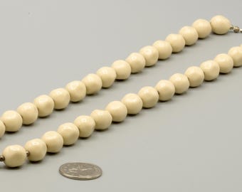 May include: A necklace composed of smooth, round, off-white beads strung together in a single strand. The beads have a matte finish and are uniform in size. A small silver-toned metal clasp is visible at the end of the strand, and a US quarter coin is placed nearby for scale.