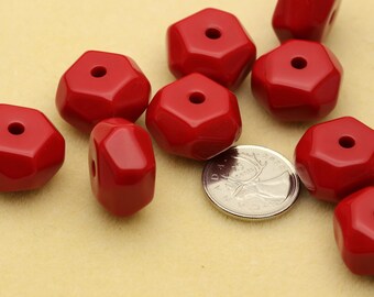 May include: A collection of ten glossy red, faceted, hexagonal beads with a central hole, arranged near a silver 25-cent coin for scale. The beads have a smooth, polished finish and a geometric shape, displayed together in a group.