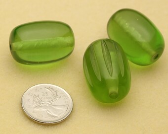 May include: Three translucent lime green glass beads with a smooth, oval shape. One bead features vertical carved grooves, while the others are plain. A Canadian 25-cent coin is placed next to the beads to provide a clear sense of scale.