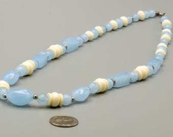 May include: A necklace featuring alternating light blue, irregularly shaped translucent beads and cream-colored, ribbed disc beads. Small silver-toned metal spacers are placed between the beads. A US quarter coin is shown for scale.