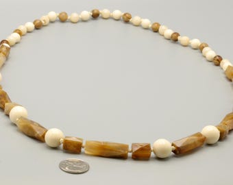 May include: A necklace featuring alternating smooth cream-colored spherical beads and faceted brown translucent cylindrical beads. The necklace is displayed next to a United States quarter coin for scale, showing the size of the beads.