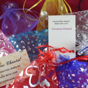 May include: An assortment of small, colorful organza bags filled with jewelry, some adorned with star and heart patterns. The image includes business cards with the text "Cr&eacute;ations Chantal, Handcrafted Jewelry, Made with Love."