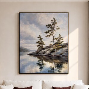 May include: A large rectangular framed wall art print depicting a landscape scene with pine trees on a rocky shoreline overlooking a calm lake under a cloudy sky. The painting features shades of blue, grey, brown, and green with soft light reflections.