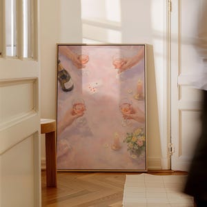 May include: A framed rectangular wall art print depicting a soft-toned scene of four hands holding wine glasses filled with a pink beverage around a table. The table features a bottle of wine, playing cards, two lit candles, and a small bouquet of flowers.