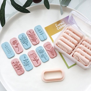 May include: A set of floral-themed cookie cutters in a clear plastic case. The cutters are in the shape of rectangles with various embossed floral designs in pink and blue. The text "formii Cutter" is visible on a yellow card.