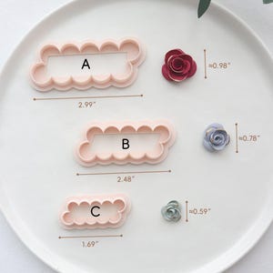 May include: Three pink plastic flower-shaped cookie cutters labelled A, B, and C, with dimensions of 7.6 cm, 6.3 cm, and 4.3 cm respectively. Three small, decorative paper flowers in red, blue, and green are also shown, with approximate diameters of 2.5 cm, 2 cm, and 1.5 cm.