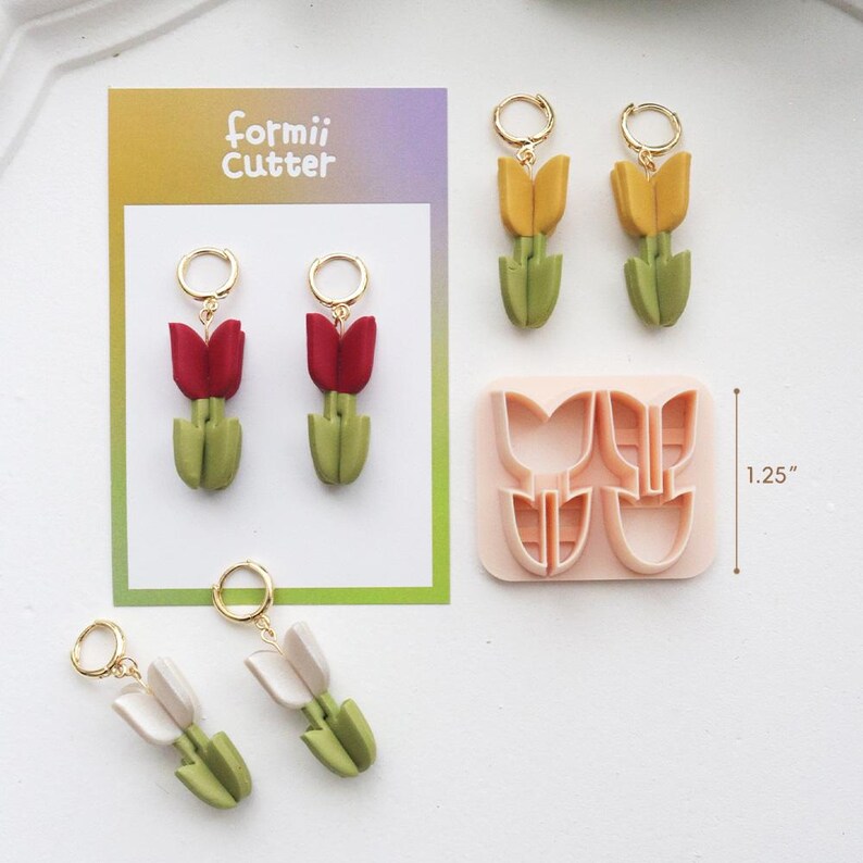 May include: Handmade tulip earrings in red, yellow, and white, with gold hoops. A pink cutter mold is also shown, measuring 3.18 cm. The earrings and mold are displayed on a white surface.