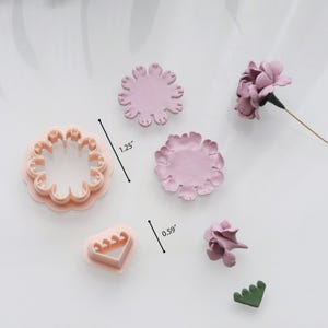 May include: A collection of pink flower-shaped cookie cutters and clay flowers. The largest cutter measures 1.25 inches in diameter. The clay flowers are in various stages of completion, with one fully formed flower and a few petals.
