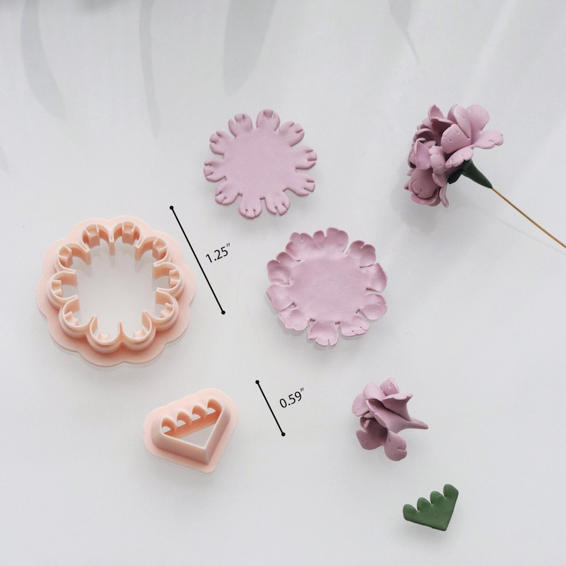 May include: A collection of pink flower-shaped cookie cutters and clay flowers. The largest cutter measures 1.25 inches in diameter. The clay flowers are in various stages of completion, with one fully formed flower and a few petals.