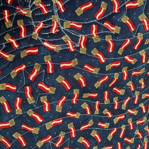 May include: A blue fabric with a repeating pattern of red, white, and gold flags. The flags are arranged in a diagonal pattern and are sewn onto the fabric.