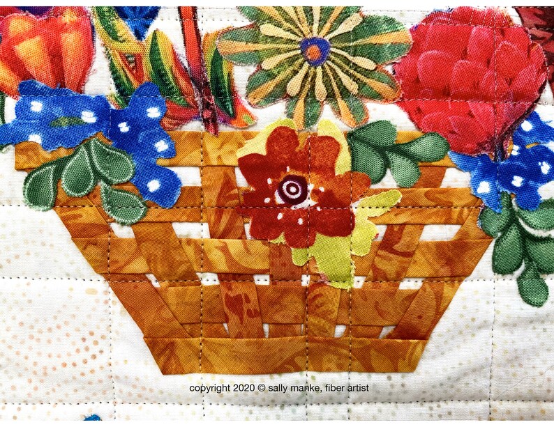 Puede incluir: Primer plano de una cesta tejida de tela llena de flores de tela de colores. La cesta est&aacute; hecha de tela marr&oacute;n y naranja y est&aacute; acolchada con hilo marr&oacute;n. Las flores est&aacute;n hechas de varias telas, incluyendo rojo, amarillo, azul y verde. El texto "copyright 2020 &copy; sally manke, fiber artist" es visible en la parte inferior de la imagen.