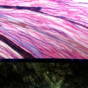 May include: A close-up of a pink and purple fabric with a dark blue border. The fabric has a quilted design with pink and purple stitching.