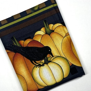 May include: A black crow perched on a pumpkin with three other pumpkins in the background. The pumpkins are yellow, orange, and brown. The background is a dark blue with a green and brown patterned border.
