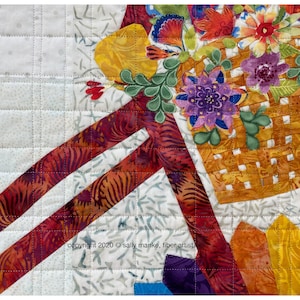 Puede incluir: Primer plano de una obra de arte de tela acolchada que presenta una cesta llena de flores coloridas. La cesta est&aacute; tejida con una tela marr&oacute;n y amarilla y las flores est&aacute;n hechas de varias telas en tonos de rojo, naranja, amarillo, morado y verde. El fondo es una tela acolchada blanca con un patr&oacute;n sutil.