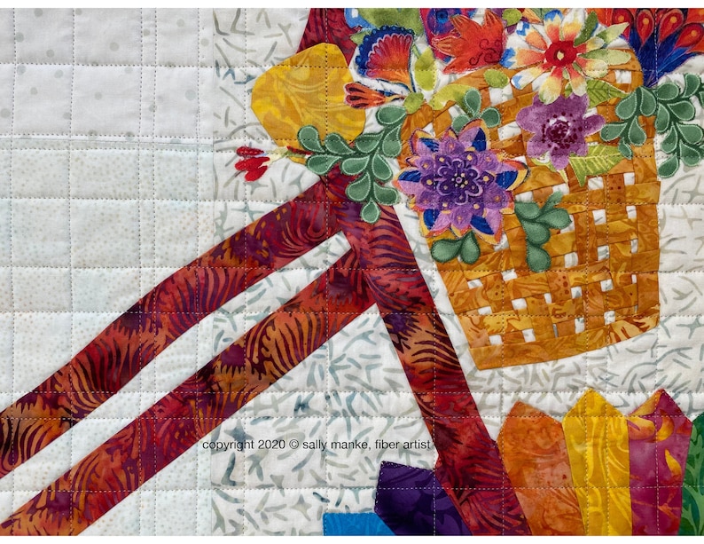 Puede incluir: Primer plano de una obra de arte de tela acolchada que presenta una cesta llena de flores coloridas. La cesta est&aacute; tejida con una tela marr&oacute;n y amarilla y las flores est&aacute;n hechas de varias telas en tonos de rojo, naranja, amarillo, morado y verde. El fondo es una tela acolchada blanca con un patr&oacute;n sutil.