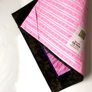 May include: A pink and white striped fabric with a white lace trim and small pink hearts. The fabric has a label that reads "Fiber artist Sally Manke, art quilts, Michigan, sallymanke.etsy.com".