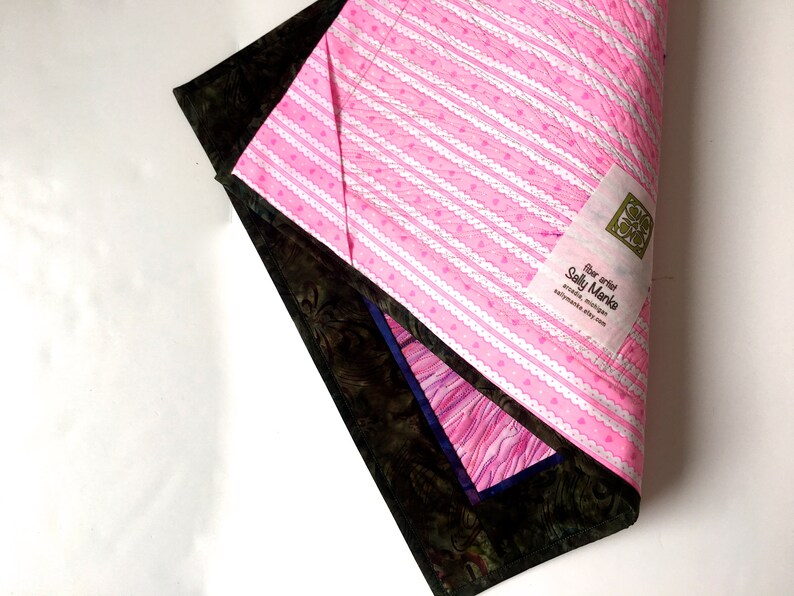 May include: A pink and white striped fabric with a white lace trim and small pink hearts. The fabric has a label that reads "Fiber artist Sally Manke, art quilts, Michigan, sallymanke.etsy.com".