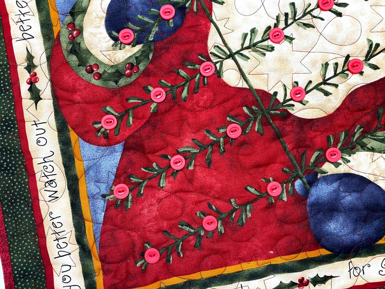 Exquisitely quilted vintage advent calendar featuring Santa Claus holding a Christmas Tree. Twenty-four buttons have been securely stitched to hang the cotton and felt ornaments day each day leading up to Christmas. Nancy Halverson holiday panel.