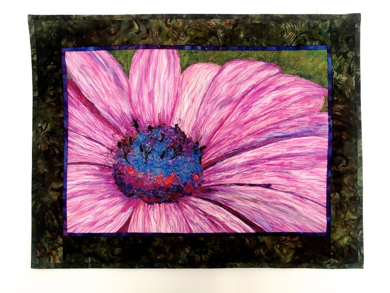 May include: A close-up of a pink flower with a blue and purple centre. The flower is surrounded by a dark green frame.