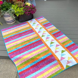 May include: A colorful striped quilt with a white border and a pattern of green, yellow, and blue triangles along one edge.